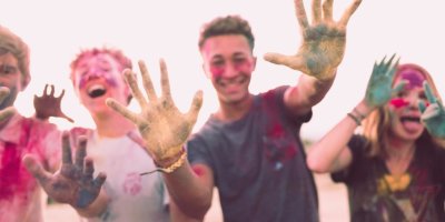 Teens with paint on their hands and faces and clothing laughing and smiling at the camera
