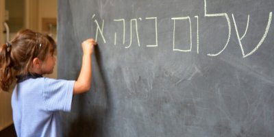 A girl writes Hebrew on a chalkboard
